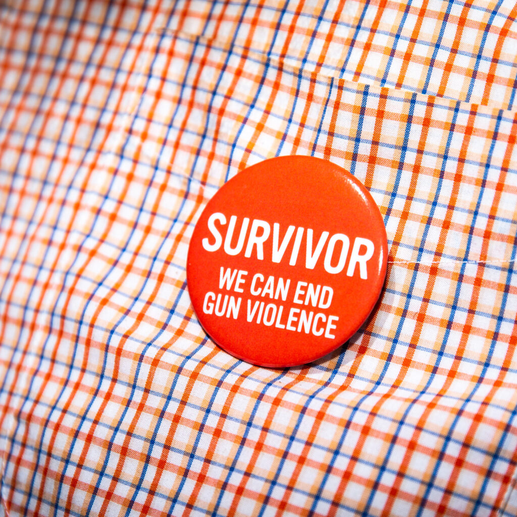 A close-up of a button on a shirt. The button reads: “Survivor. We can end gun violence”