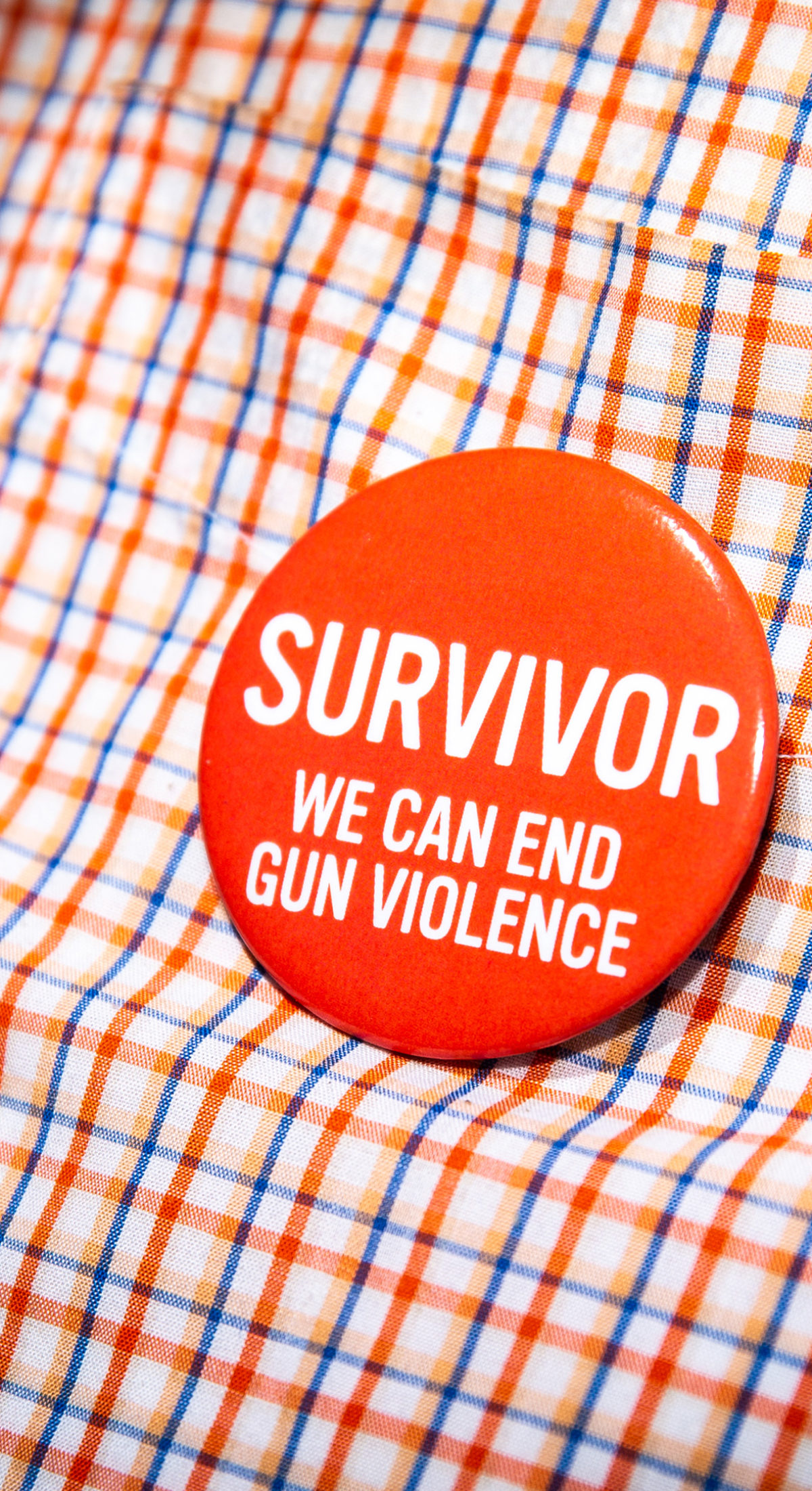 A close-up of a button on a shirt. The button reads: “Survivor. We can end gun violence”
