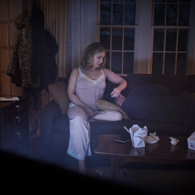 A woman sits on a couch and stares at a person laying on the couch with her
