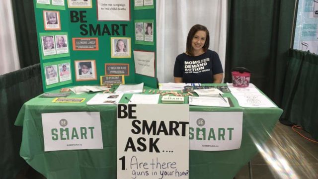 A Moms Demand Action volunteer sits at a table with Be SMART information