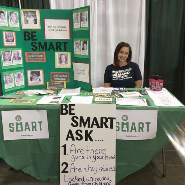 A Moms Demand Action volunteer sits at a table with Be SMART information