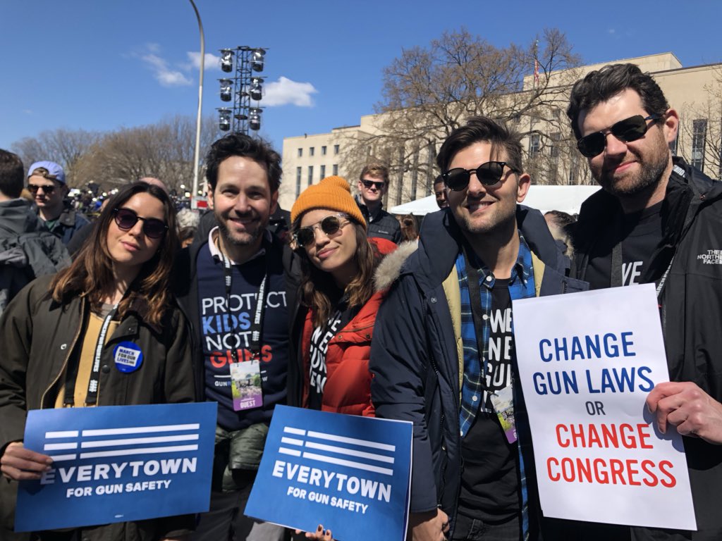 A group of people, including Paul Rudd, Adam Scott, and Billy Eichner smile while holding Everytown signs at a march