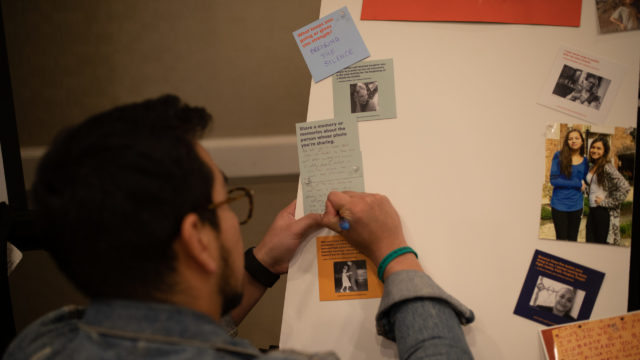 A woman pins a moment that survives post it to a board with images of those lost to gun violence