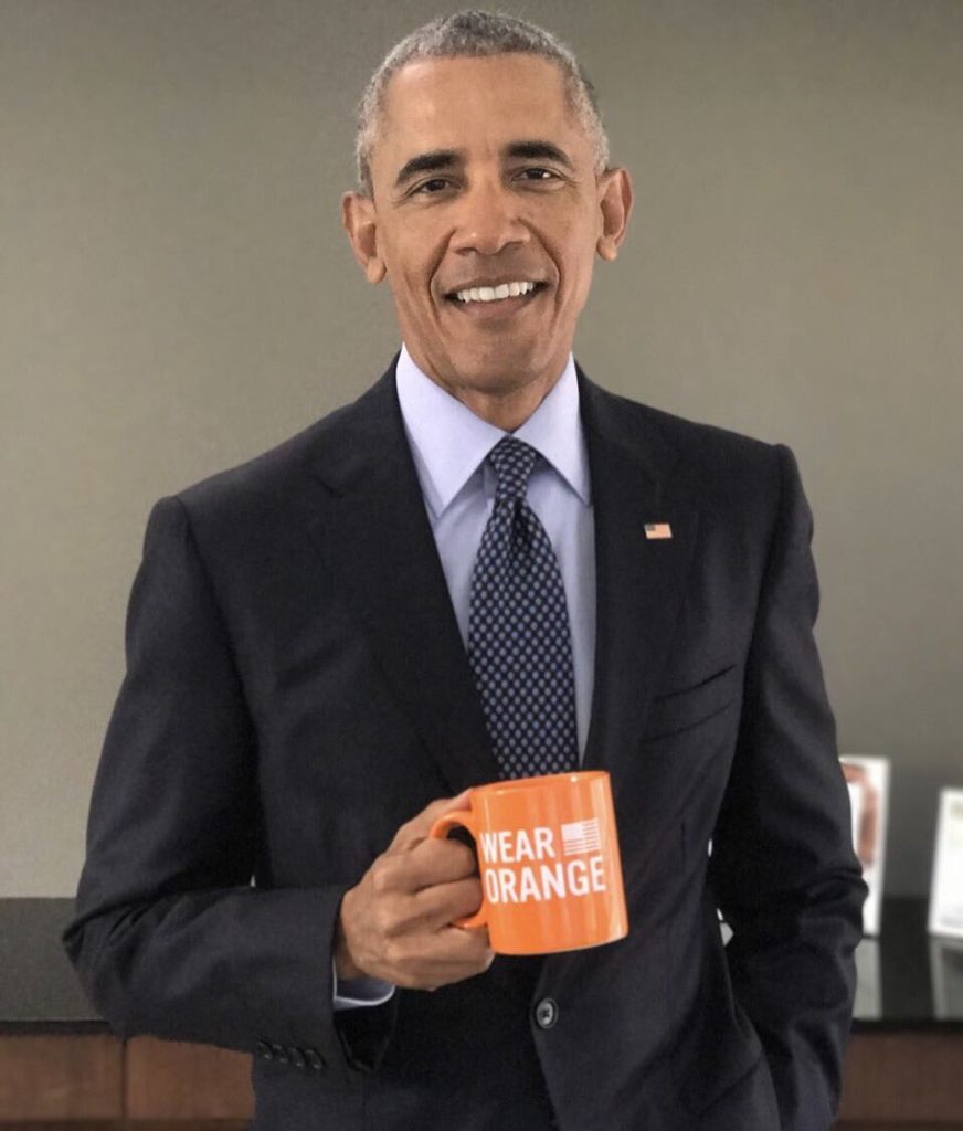 President Barrack Obama smiles while holding a Wear Orange mug