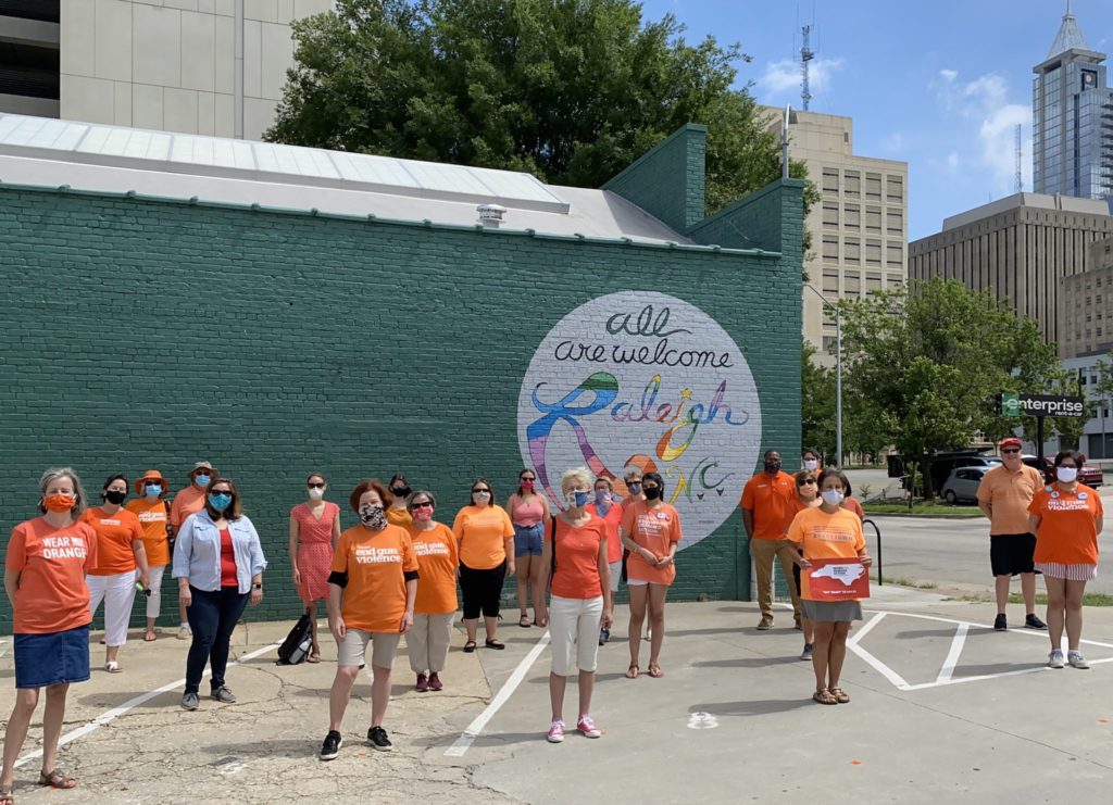 A group of 20 volunteers stand in front of a mural in Raleigh, NC while wearing Wear Orange shirts and masks while socially distancing during the pandemic