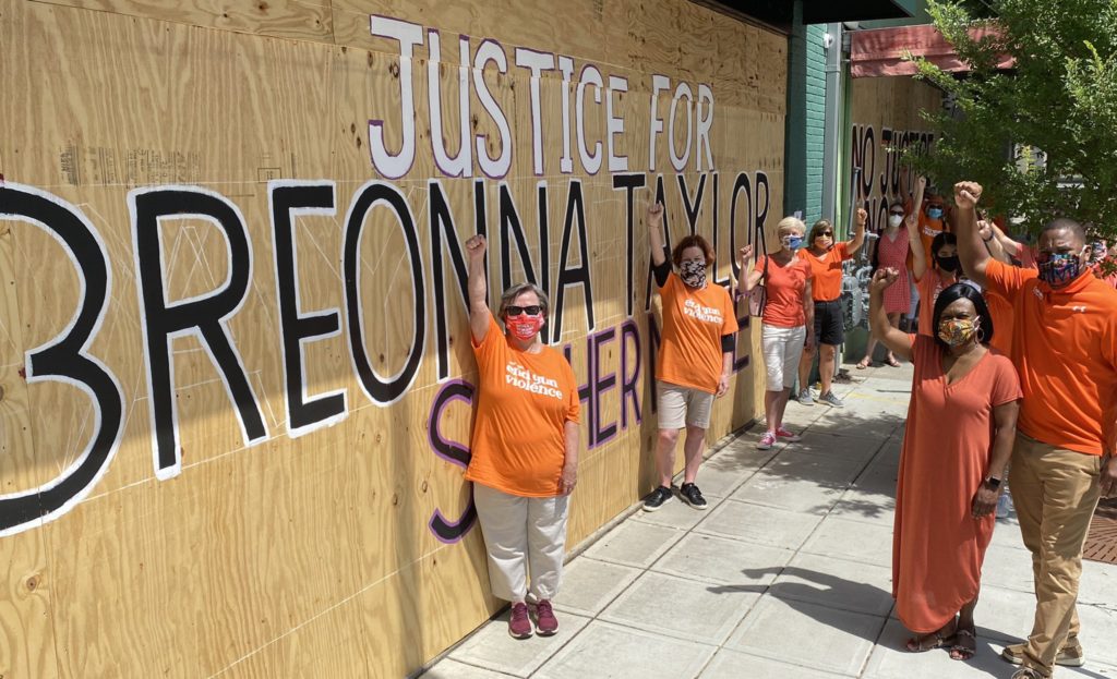 Volunteers in Raleigh wear orange while standing in front of a 'justice for Breonna Taylor' mural