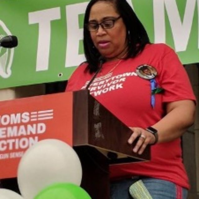 Regina Thompson-Jenkins standing before a podium wearing a red Everytown Survivor Network shirt