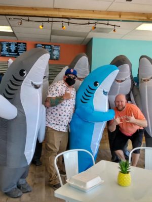 Jeremy Bay, Executive Director of Grace for 2 Brothers Foundation, smiles at an event with a group of people dressed in shark costumes