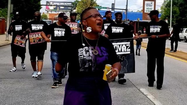 Erricka marches at the front of a protest with other Ceasefire Baltimore volunteers behind her, holding a banner.