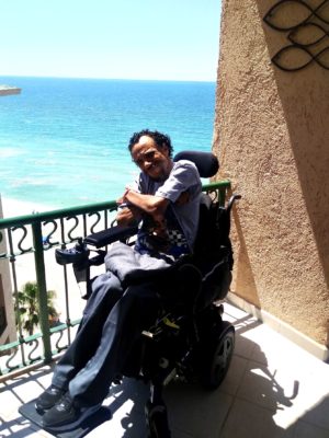 James Hinckley Wade smiles in his wheelchair with a beach in the background