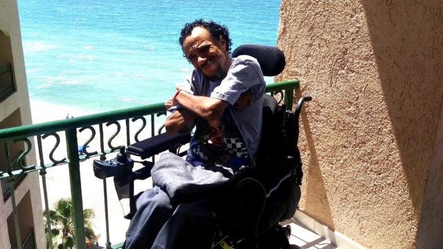 James Hinckley Wade smiles in his wheelchair with a beach in the background