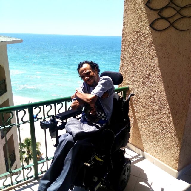 James Hinckley Wade smiles in his wheelchair with a beach in the background