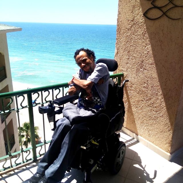 James Hinckley Wade smiles in his wheelchair with a beach in the background