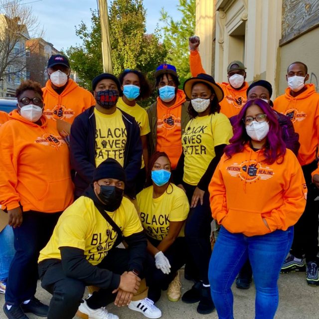 A group of 14 people from Paterson Healing Collective in New Jersey pose together while wearing orange sweatshirts or Black Lives Matter t-shirts and masks during the COVID-19 pandemic