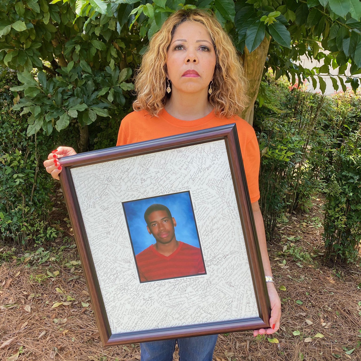 Georgia Representative Lucy McBath wear an orange shirt while holding up a photo of her son Jordan