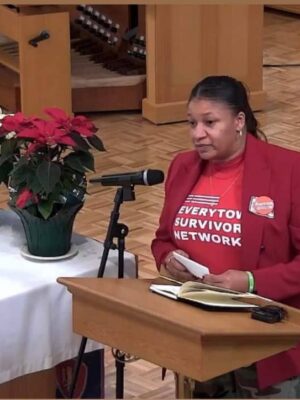 Donnitta Marie Sinclair wearing a red Everytown Survivor Network t-shirt and speaking at a podium