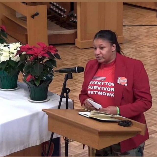 Donnitta Marie Sinclair wearing a red Everytown Survivor Network t-shirt and speaking at a podium
