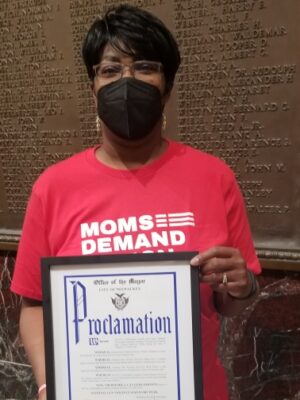 Jenevia Blanks holding a framed proclamation from the Office of the Mayor
