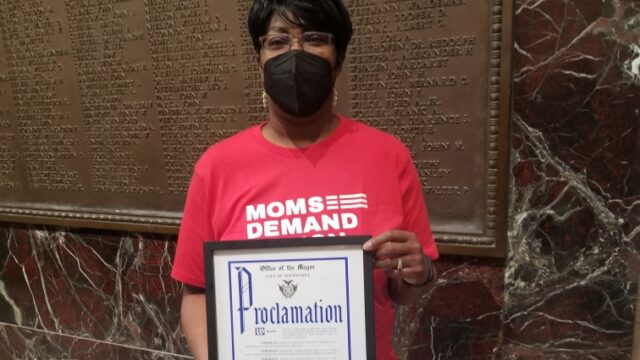 Jenevia Blanks holding a framed proclamation from the Office of the Mayor