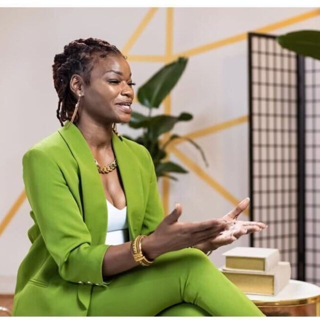Lolita Frazier seated while speaking and dressed in a lime green pantsuit