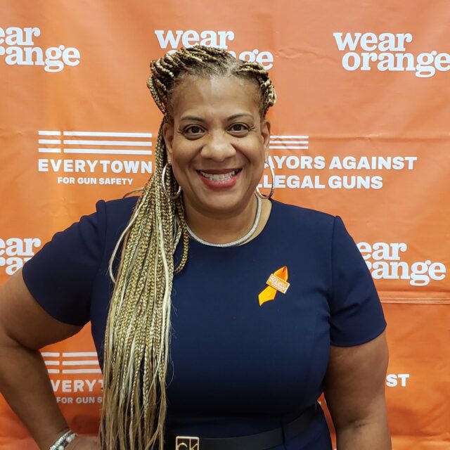 Mayor Shawyn Patterson-Howard wearing an orange ribbon in front of a Wear Orange backdrop