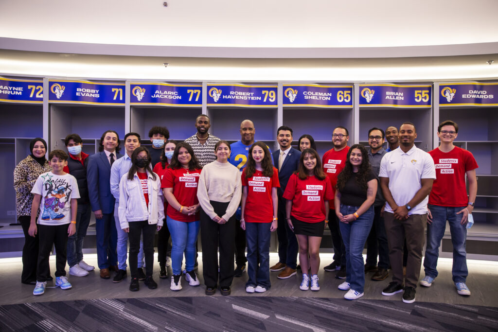 Students Demand Action volunteers pose for a photo with Rams players in the Rams' locker room at SoFi Stadium