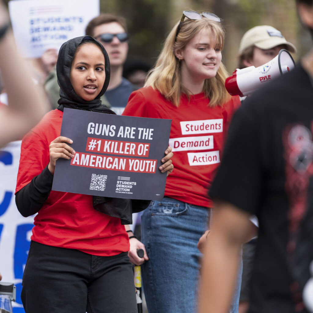 A Students Demand Action volunteer holds a sign that says “Guns are the #1 killer of American youth”