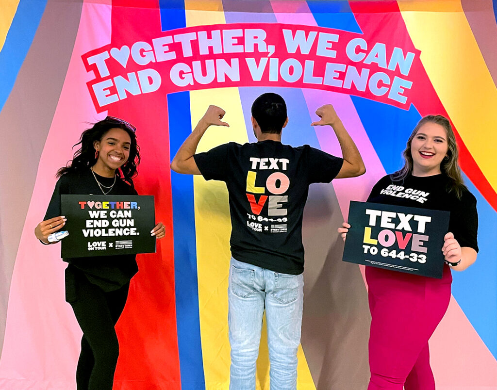 Everytown staff members pose for a photo in their Harry Styles x Love on Tour t-shirts and in front of a “Together, We Can End Gun Violence” backdrop