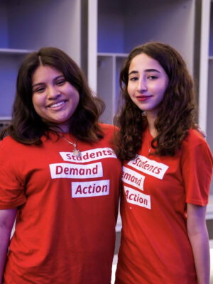 Ashley Castillo poses for a photo with another Students Demand Action volunteer. They are both wearing red Students Demand Action t-shirts.