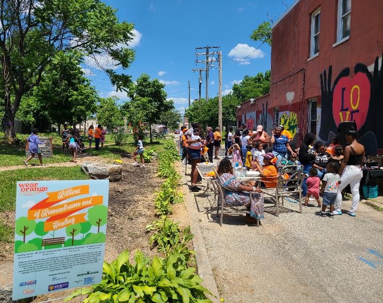 Sandtown community members gather at a pocket park in Baltimore, MD. A Wear Orange sign is visible in the foreground.