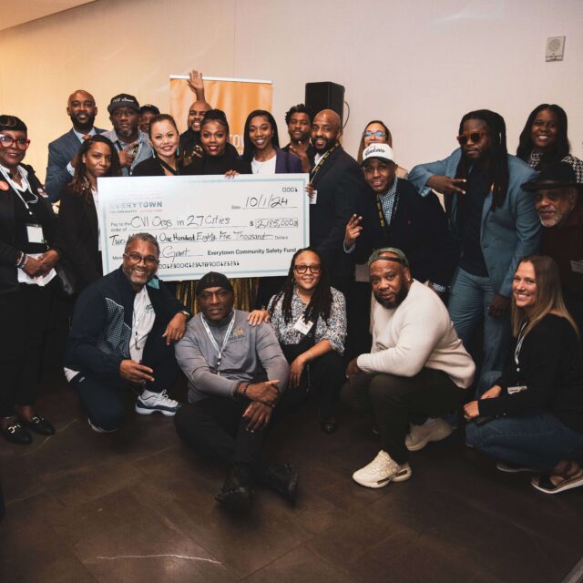 A group of grantees pose with Community Safety Fund team members for a photo. Several people are holding a large check that reads: