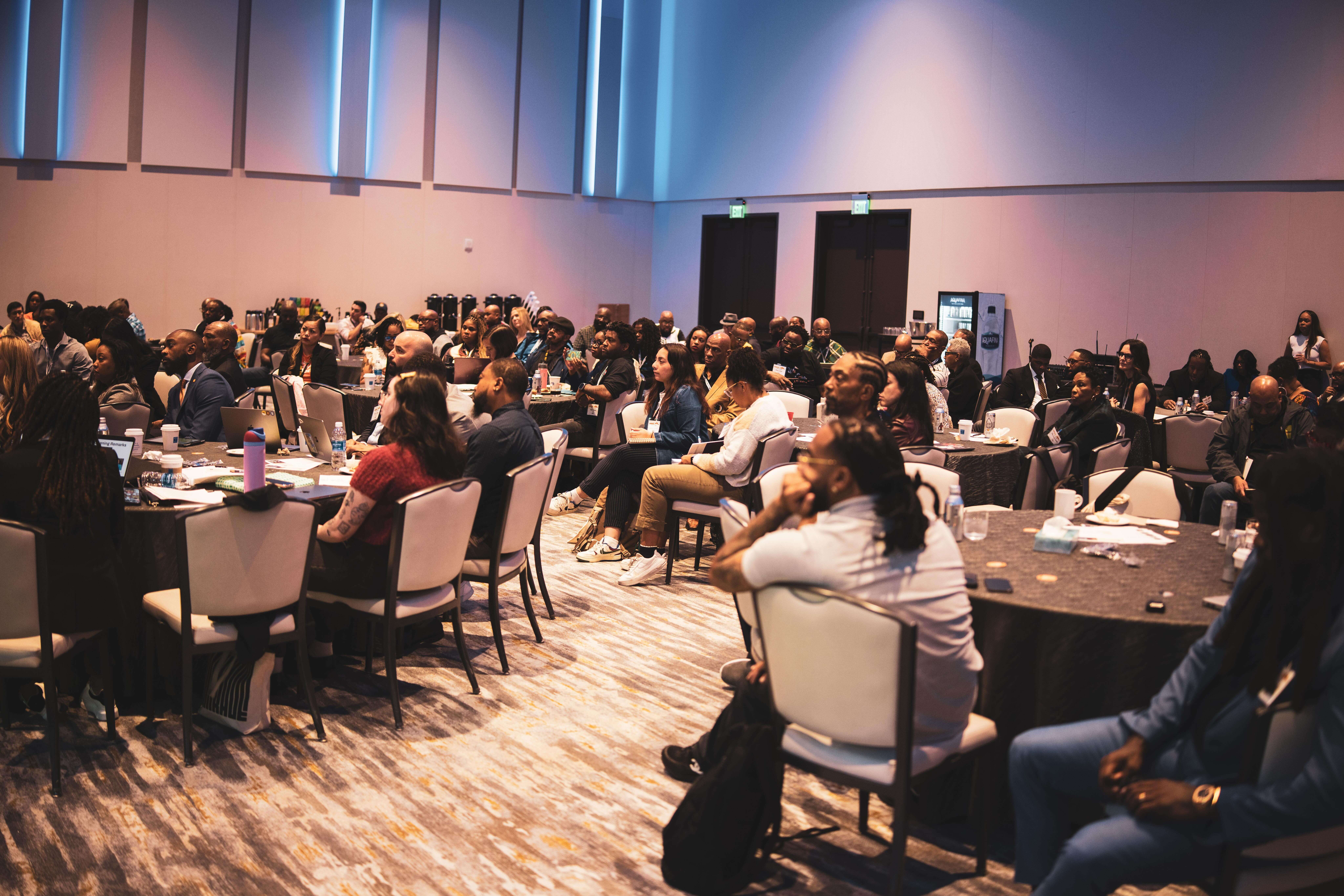 A candid photo of a room full of Community Safety Fund grantees at the Everytown Pre-Institute at the Cities United conference. Attendees are sitting at circular tables and spread throughout the room.