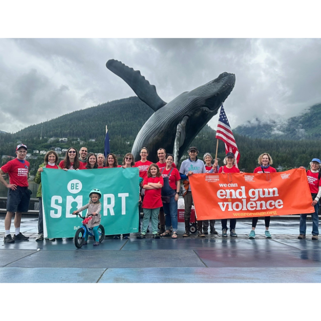 Be SMART volunteers pose for a photo in Alaska. They are wearing red Moms Demand Action shirts and holding two banners, one that reads