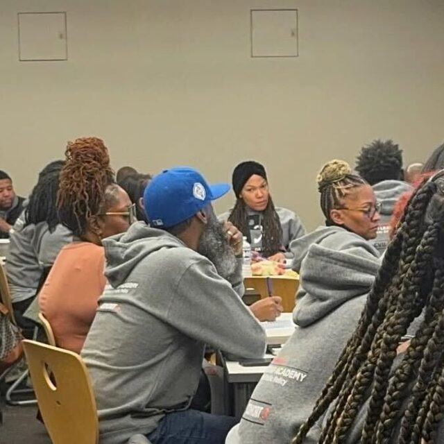 A candid photo of Michael-Sean Spence, a Black man wearing light dress pants and a dark long-sleeve shirt, teaching a room full of community violence intervention practitioners during a training at the University of Chicago's Community Violence Intervention Leadership Academy.