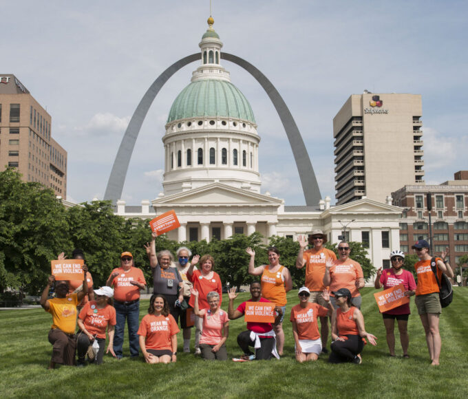 Supportes in orange shirts in front of the Old Courthouse and St. Louis Arch